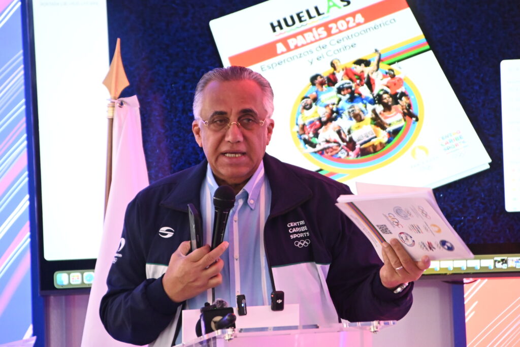 Luis Mejía Oviedo, presidente de Centro Caribe Sports, sostiene un ejemplar del libro "HUELLAS A PARIS 2024", durante el acto con los Comités Olímpicos Nacionales y los medios. (Centro Caribe Sports)